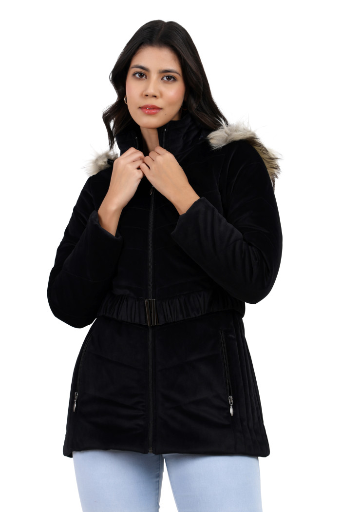 A woman in a relaxed standing pose wears Coatsnmore’s black velvet quilted jacket, featuring a mandarin collar, removable hood, adjustable waistband zip closure, concealed zippered side pockets and blue jeans with both hands on collar.